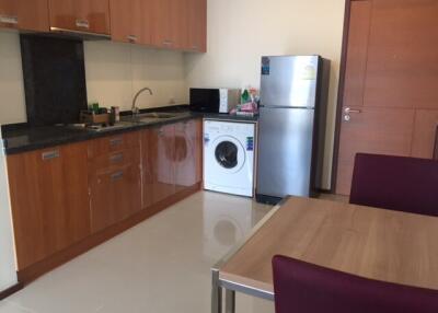 Modern kitchen area with wooden cabinets, granite countertops, a refrigerator, and a washing machine.