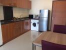 Modern kitchen area with wooden cabinets, granite countertops, a refrigerator, and a washing machine.