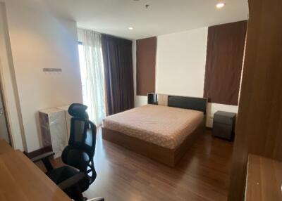 Spacious and modern bedroom with a large bed, office chair, and ample natural light from large window