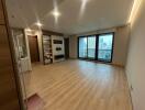 Spacious living room with wooden flooring, large window, storage units, and a small kitchenette