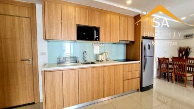 Modern kitchen with wooden cabinets, modern appliances, including a refrigerator and microwave, and a dining area.