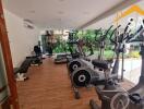 Well-equipped gym with modern exercise machines and large windows overlooking a garden