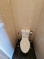 Modern bathroom with tiled walls and floor, featuring a toilet and a bidet hose