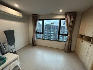 Well-lit bedroom with wooden flooring, large window with city view, and built-in wardrobe