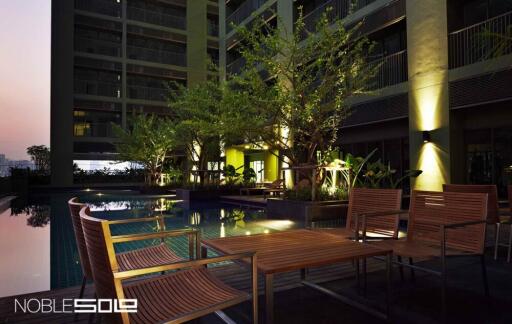 Outdoor pool area at a residential building with wooden furniture and lighting