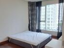 Bedroom with a mattress, large window, and a view of high-rise buildings