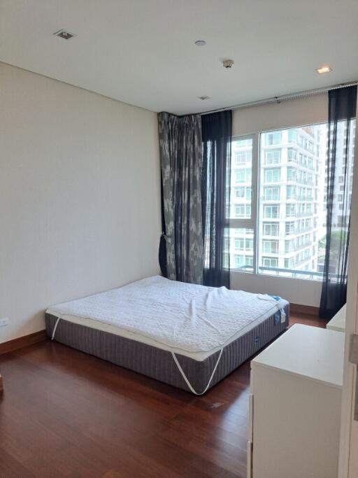 Bedroom with a mattress, large window, and a view of high-rise buildings