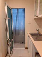 Small kitchen with a sink, counter space, storage cabinets, and a door to an attached shower area