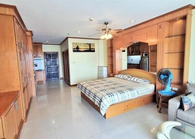 Spacious bedroom with built-in wooden cabinets, bed with checkered bedding, ceiling fan, and adjacent living area