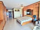 Spacious bedroom with built-in wooden cabinets, bed with checkered bedding, ceiling fan, and adjacent living area