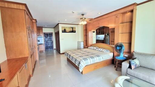 Spacious bedroom with built-in wooden cabinets, bed with checkered bedding, ceiling fan, and adjacent living area