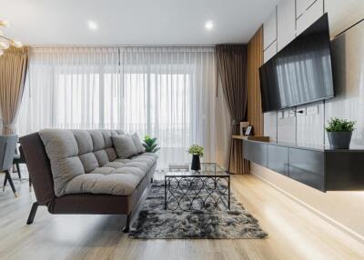 Modern living room with a sofa, wall-mounted TV, and large windows