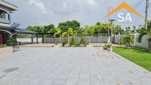 Spacious paved outdoor area with greenery and a modern building in the background