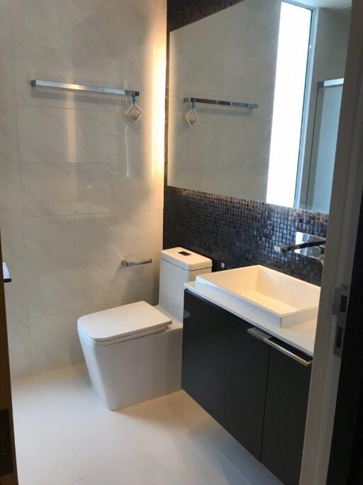 Modern bathroom with a sink, toilet, large mirror, and towel racks