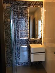 Modern bathroom with mosaic tile wall, glass shower door, and floating sink