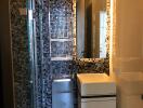 Modern bathroom with mosaic tile wall, glass shower door, and floating sink