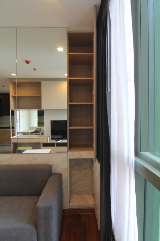 Modern living room with grey sofa, shelves, windows with curtains, and a mirrored wall