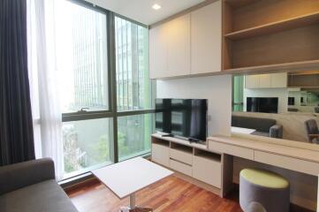 Modern living room with large windows, a flat-screen TV, and built-in shelves and drawers