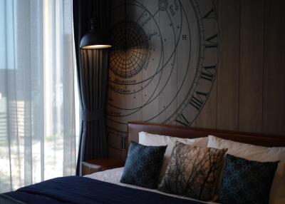 Cozy bedroom with dark blue and gray tones, a large bed with decorative pillows, a wall art piece, and a window with curtains