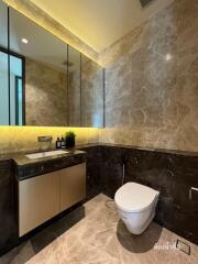 Modern bathroom with marble walls, illuminated mirror, and white toilet