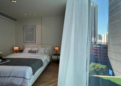 Modern bedroom with a large bed, nightstands with lamps, and a view of the city through a large window