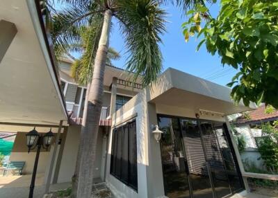 Exterior view of a modern building with large windows, surrounded by palm trees and greenery