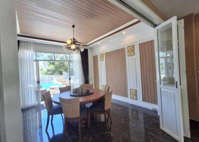 Modern dining room with a round table and chairs, near large windows and a view of a pool.