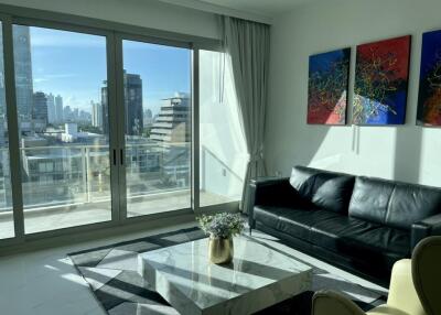 Modern living room with large windows, black leather sofa, and colorful wall art