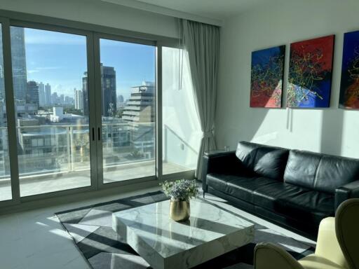 Modern living room with large windows, black leather sofa, and colorful wall art