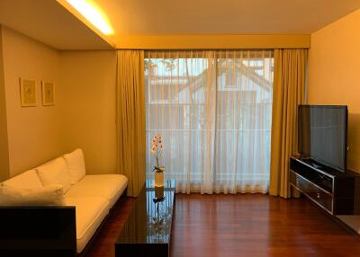 Modern living room with hardwood floor, white sofa, TV, and large window with curtains