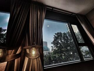 Bedroom with large windows and curtains overlooking a cityscape