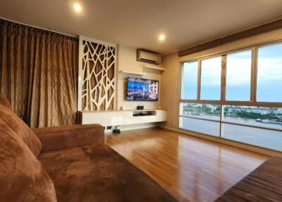 Modern living room with large windows, a wall-mounted TV, and brown furniture