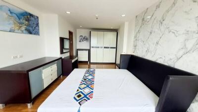 Modern bedroom with a large bed, marble accent wall, wardrobe, and chest of drawers