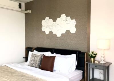 Modern bedroom with double bed, decorative hexagonal wall art, bedside table, lamp, and air conditioning