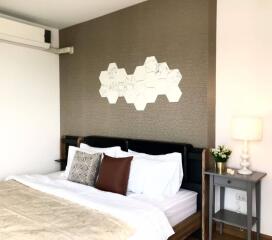 Modern bedroom with double bed, decorative hexagonal wall art, bedside table, lamp, and air conditioning