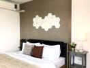 Modern bedroom with double bed, decorative hexagonal wall art, bedside table, lamp, and air conditioning