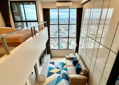 Modern loft-style living room with a mezzanine bedroom, large floor-to-ceiling windows, and a stunning city view