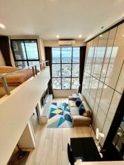 Modern loft-style living room with a mezzanine bedroom, large floor-to-ceiling windows, and a stunning city view