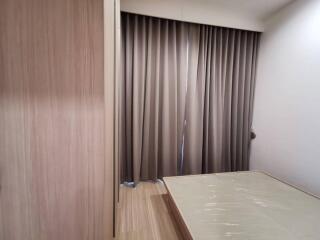 Minimalist bedroom with large window covered by curtains and wooden flooring.