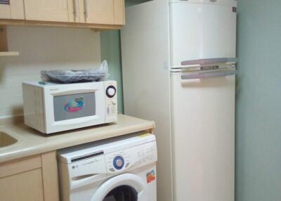 Small kitchen with refrigerator, washing machine, microwave, and wooden cabinets