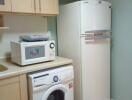 Small kitchen with refrigerator, washing machine, microwave, and wooden cabinets