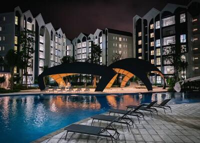 Modern apartment buildings surrounding a well-lit swimming pool area at night.