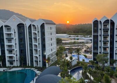 A view of a residential complex with multiple buildings, a pool, and a beautiful sunset