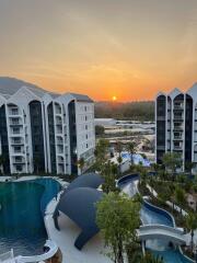 A view of a residential complex with multiple buildings, a pool, and a beautiful sunset