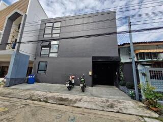 A modern grey 3-story building with two motorcycles parked in front