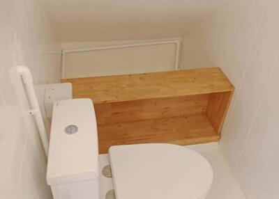 Small bathroom with white toilet and wooden shelf