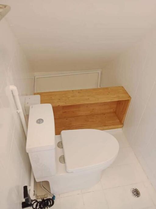 Small bathroom with white toilet and wooden shelf