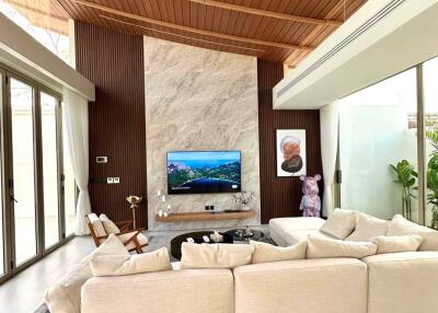 Modern living room with high wooden ceiling, marble accent wall, large sectional sofa, and wall-mounted TV