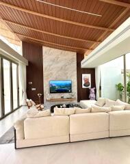 Modern living room with high wooden ceiling, marble accent wall, large sectional sofa, and wall-mounted TV