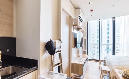 Modern bedroom with a small kitchen area, large windows, and city view